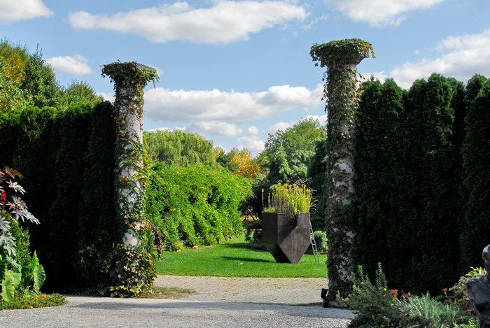Sculptures, blue sky, bushes, columns, grass